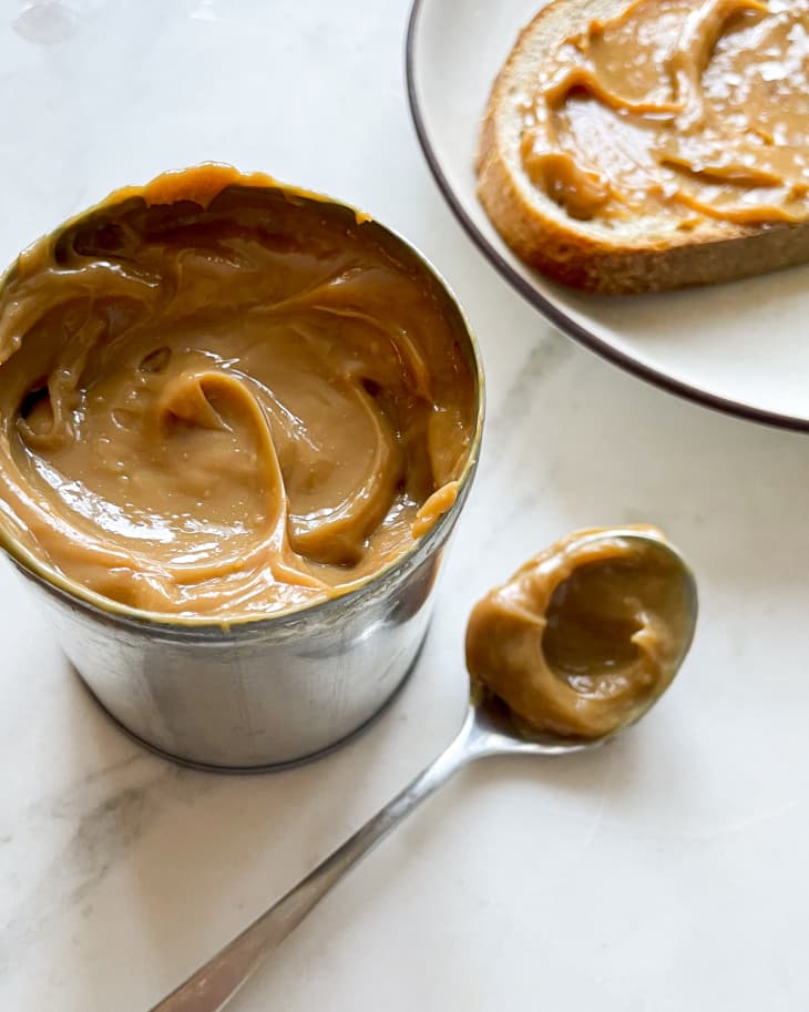 Dulce de leche (also known as caramelized milk or milk jam in English, is a confection from Latin America prepared by slowly heating sugar and milk over a period of several hours) in a small metal ramekin with a small amount on a spoon