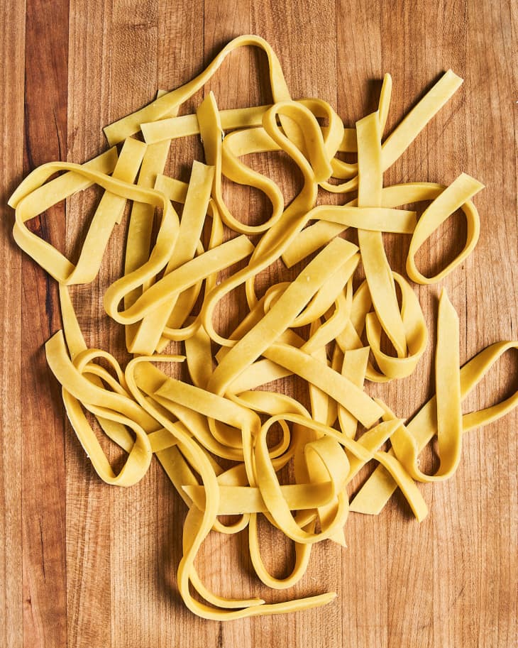 raw egg noodles (Egg noodles are noodles made with flour and eggs. The dough is rolled thin, cut into strips, and cooked in boiling water) on a wooden cutting board
