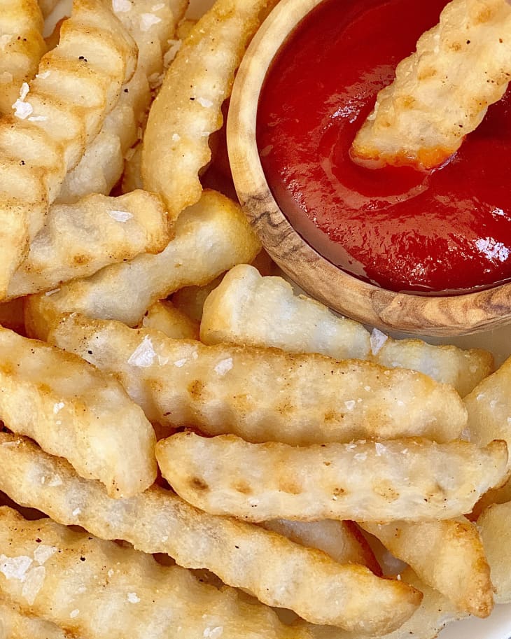 crinkle cut french fries on a plate with a small wooden ramekin of ketchup besides it on the plate