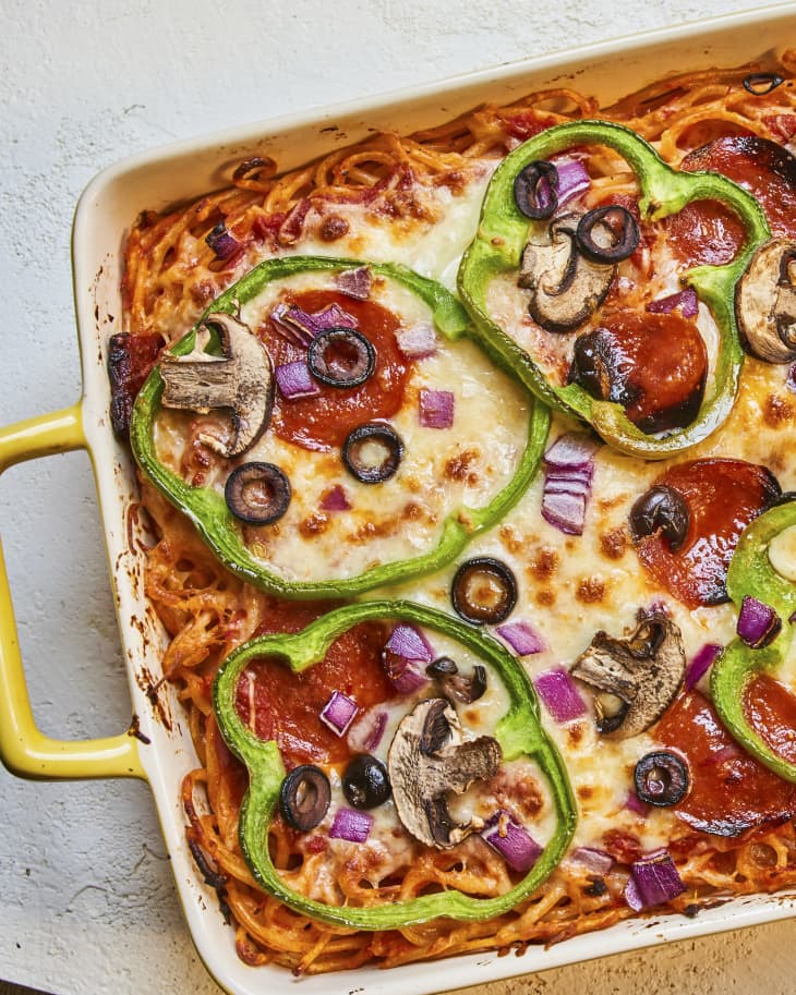 baked spaghetti with melted cheese and pizza toppings (green peppers, onions and black olives) on top