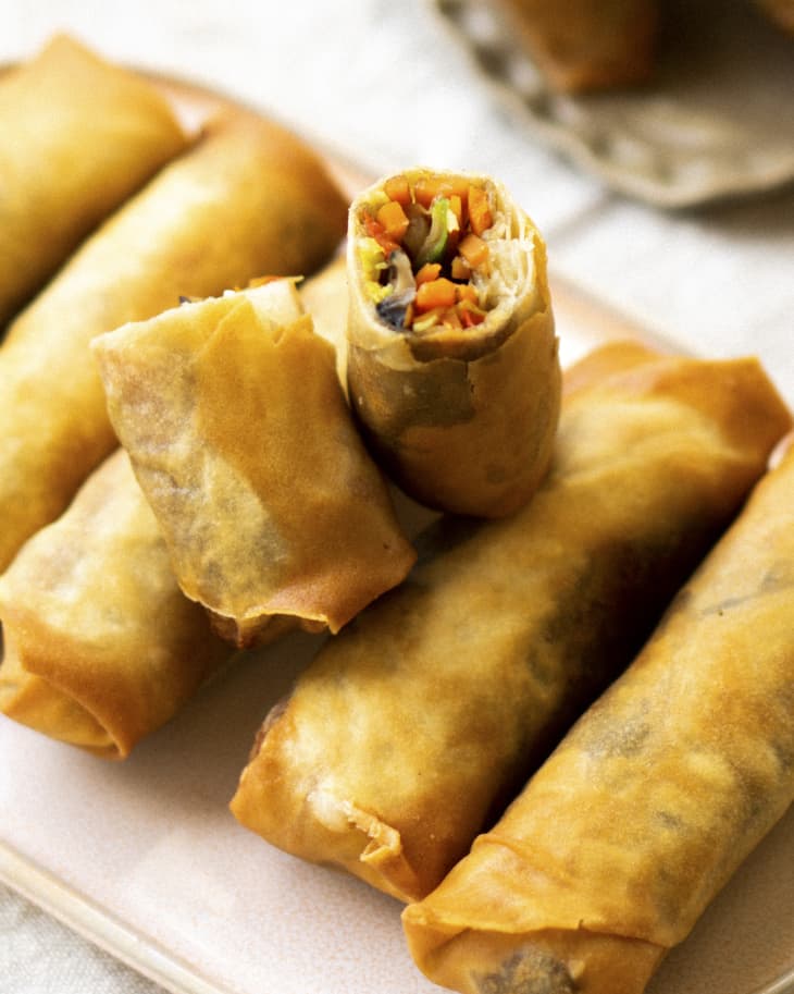 six fried vegetarian spring rolls with one cut in half and leaned on top of the others
