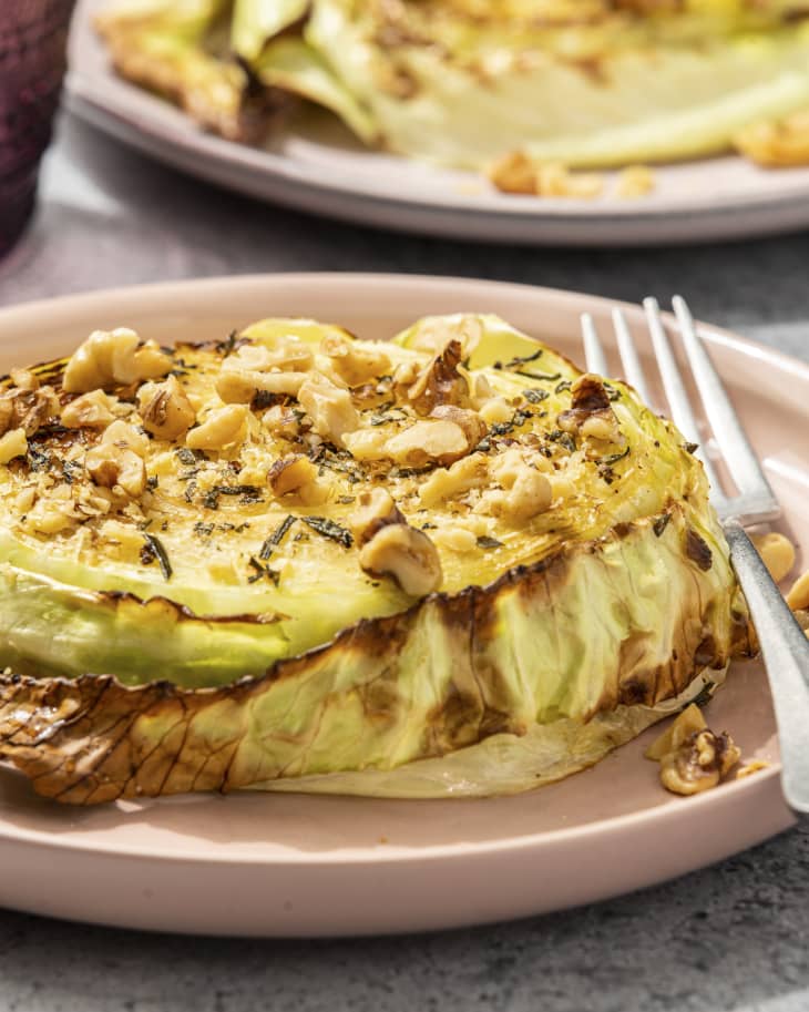 a grilled slice of cabbage on a plate with a nut topping