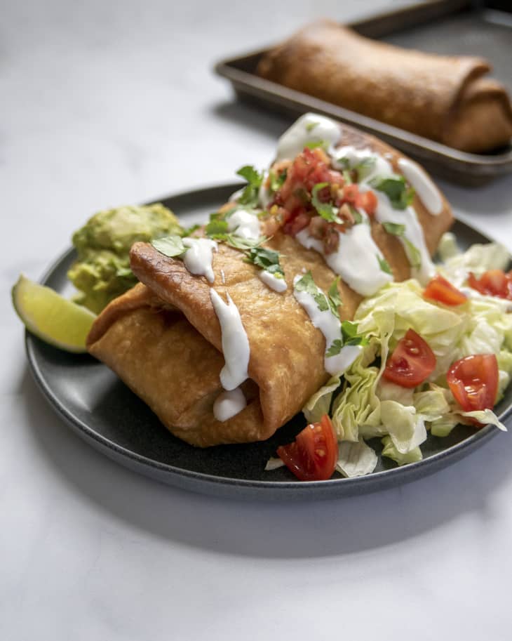 A chimichanga with sour cream, tomatoes and green garnish on top, and a salad with lettuce and tomatoes on the side.