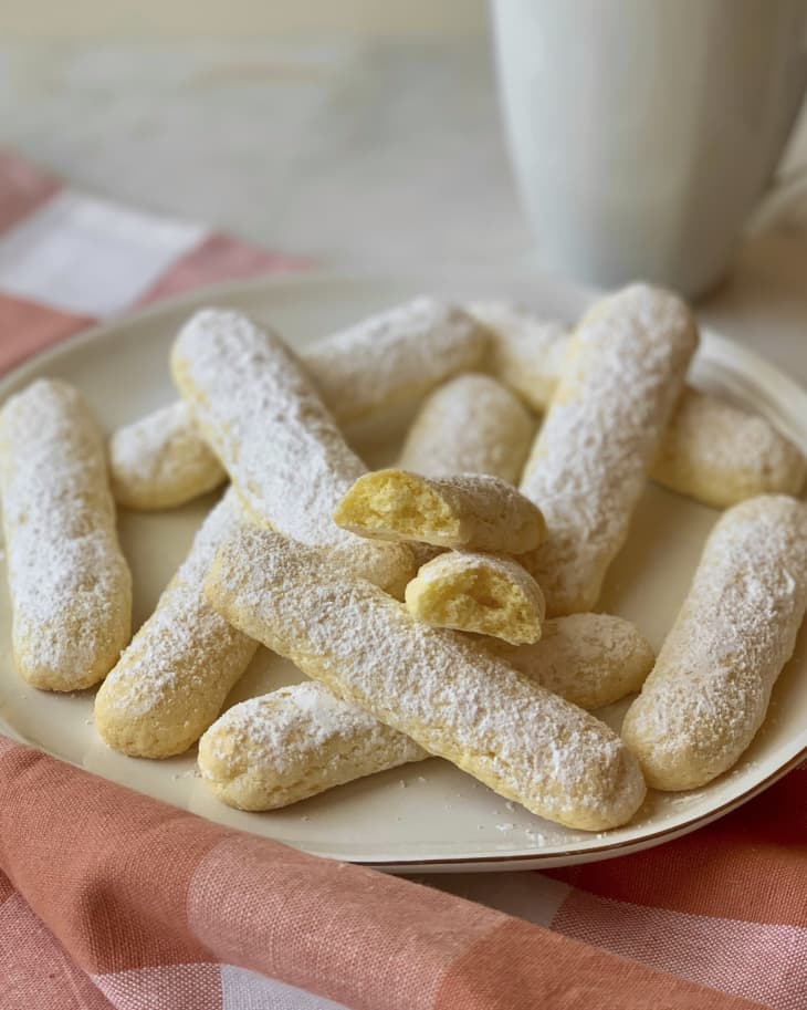 ladyfingers on a plate with a cup of coffee behind it