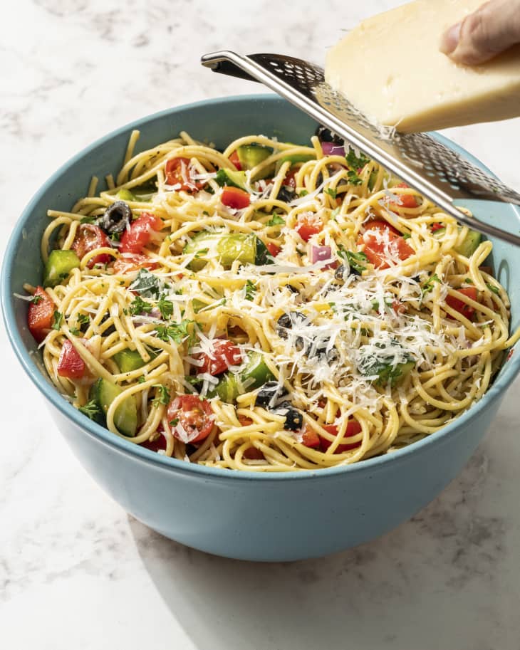 spaghetti in a bowl tossed with peppers, cucumbers, and parmesan cheese