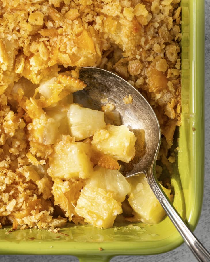 a pineapple casserole in a square, green baking dish, with a silver spoon resting inside