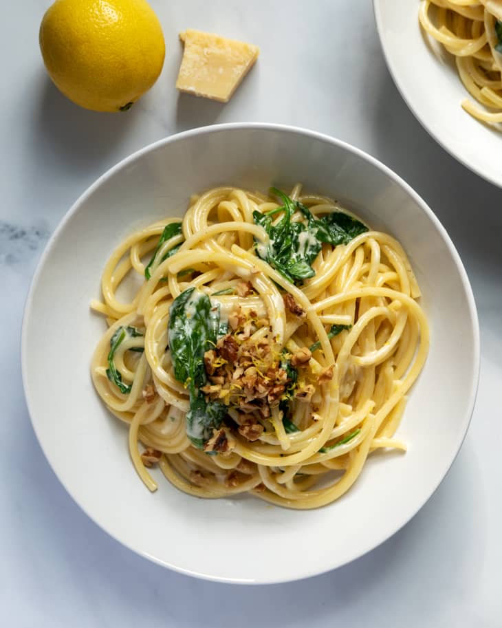linguine with spinach on a plate with lemon and piece of parmesan cheese on the side