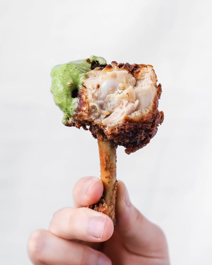 a hand holding a chicken lollipop (crispy batter-fried chicken wings made using chicken drumettes and wingettes) dipped in pale green sauce