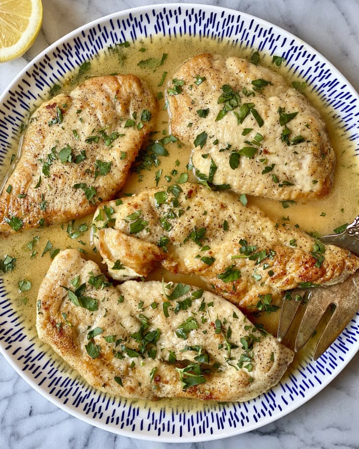 four pieces of chicken scallopini with a green garnish on a round plate with a lemon wedge in the corner