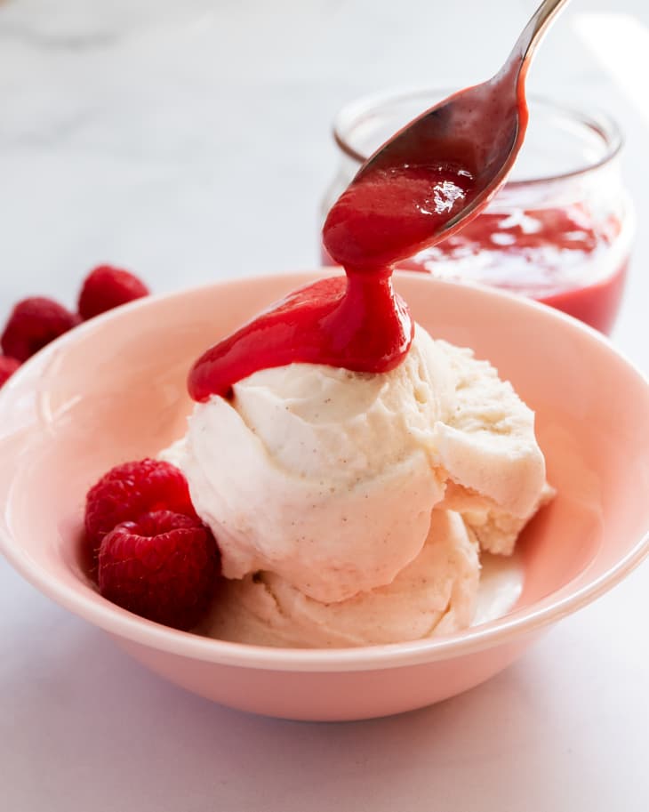 Raspberry coulis (a thin raspberry fruit puree, used as a sauce) being spooned over vanilla ice cream