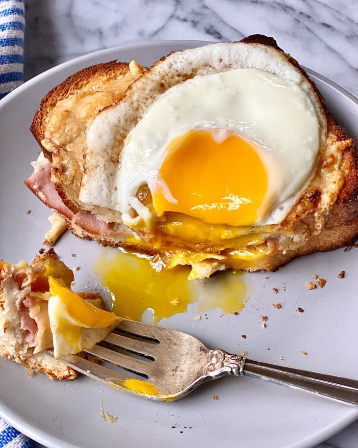 an over easy egg on two pieces of toast with the yolk running and a fork taking a bite out.