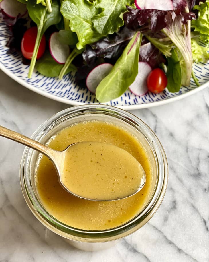 a spoon holding up a spoonful of honey mustard dressing with a salad in the background