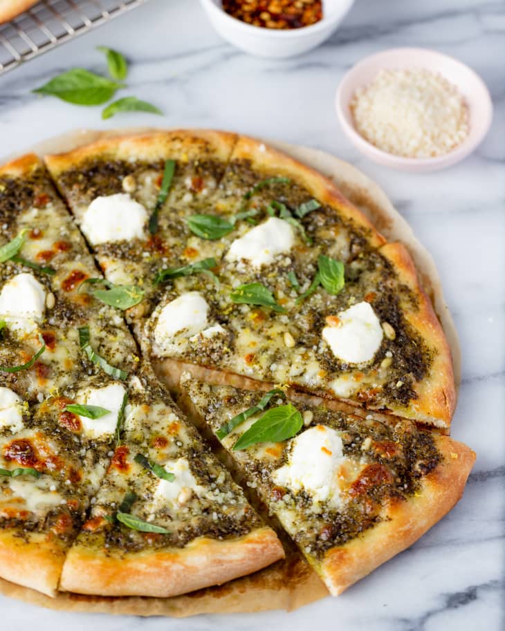 a round pizza pie with pesto sauce and pieces of white cheese