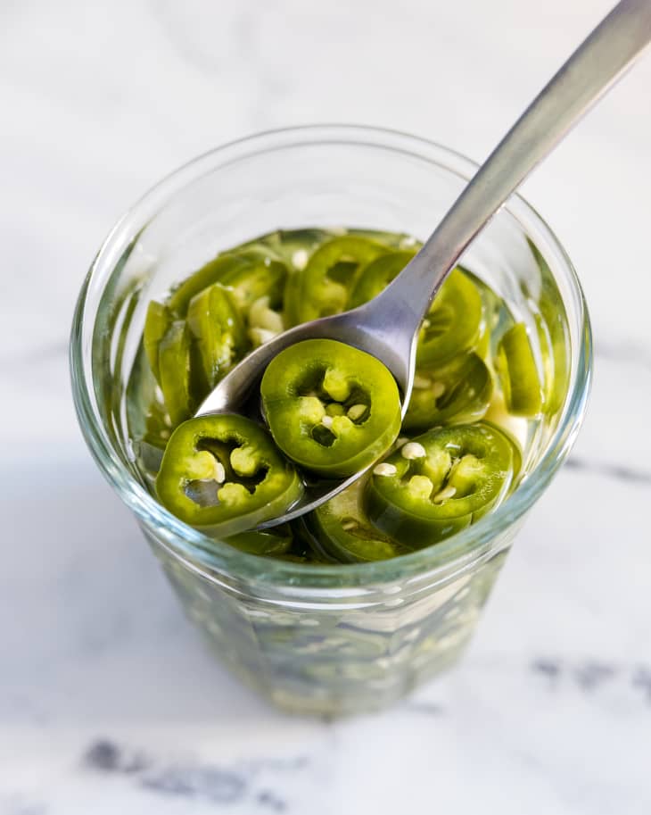 pickled jalapenos in a small glass jar, with a spoon inside