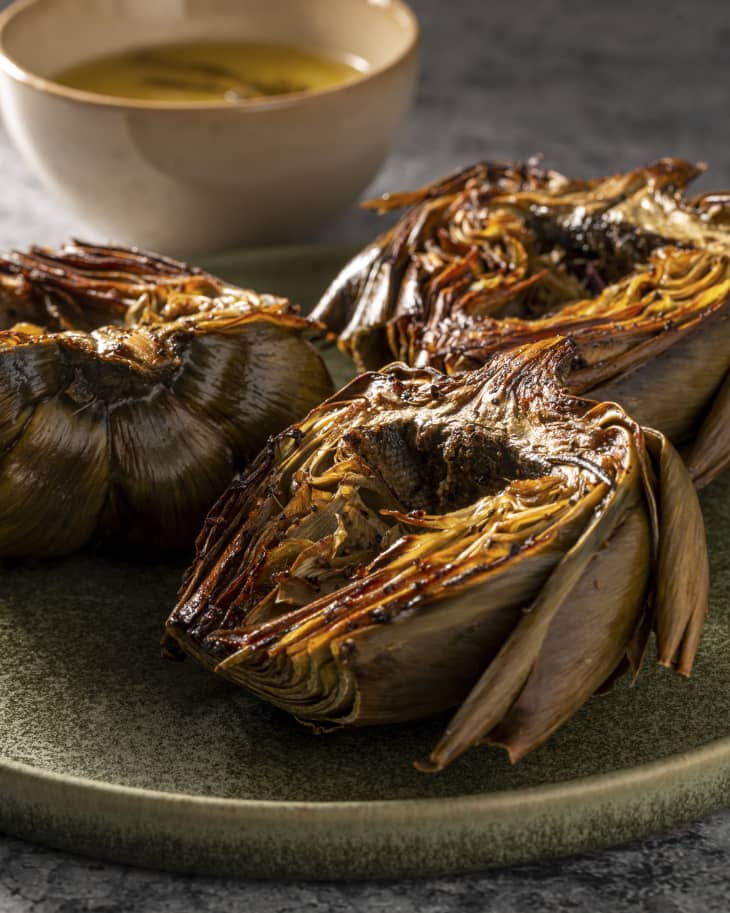 three pieces of roasted artichokes on a plate with a bowl of dipping sauce in the background