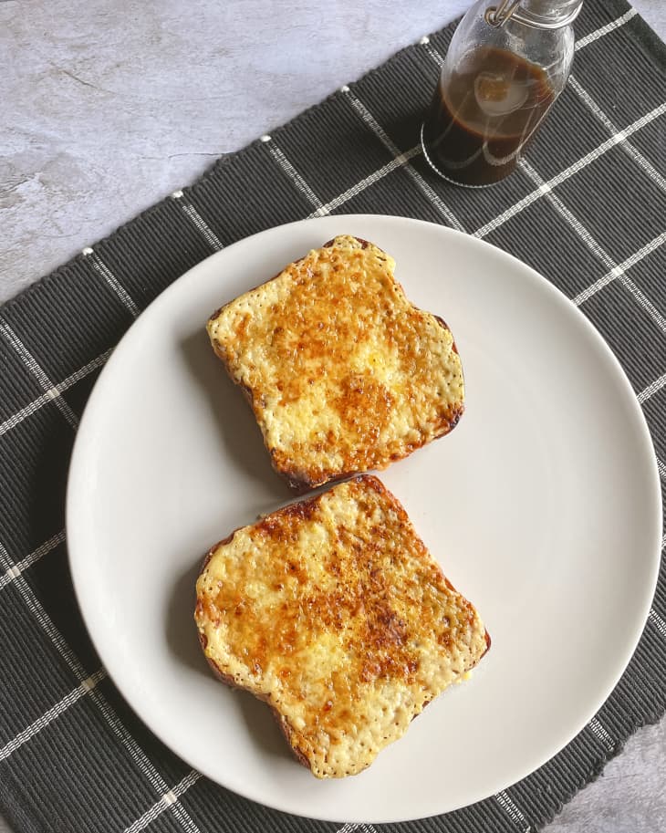 two pieces of toast with melted cheese on top, and a small bottle of brown sauce on the side.
