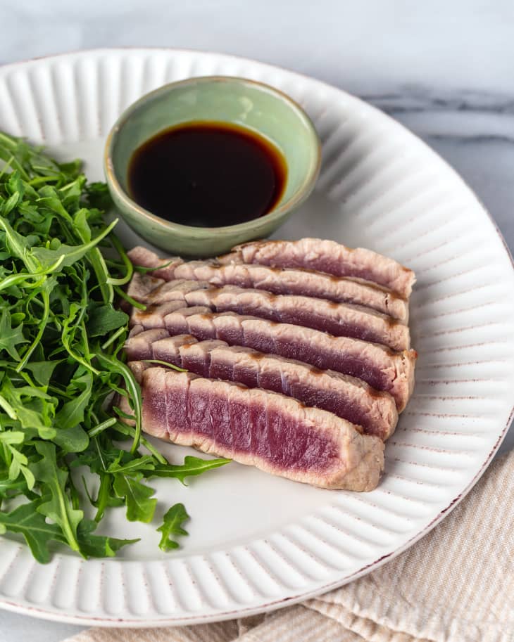 sliced, grilled tuna steak on a plate with mixed greens and a brown sauce on the side.