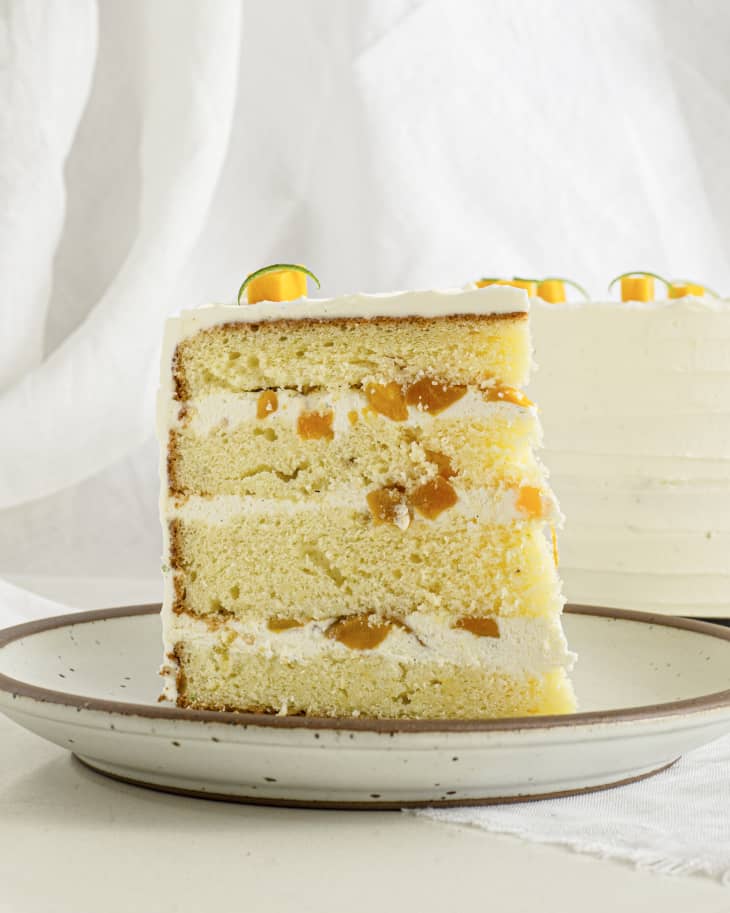a slice of white, layered cake with white frosting and chunks of mango inside.