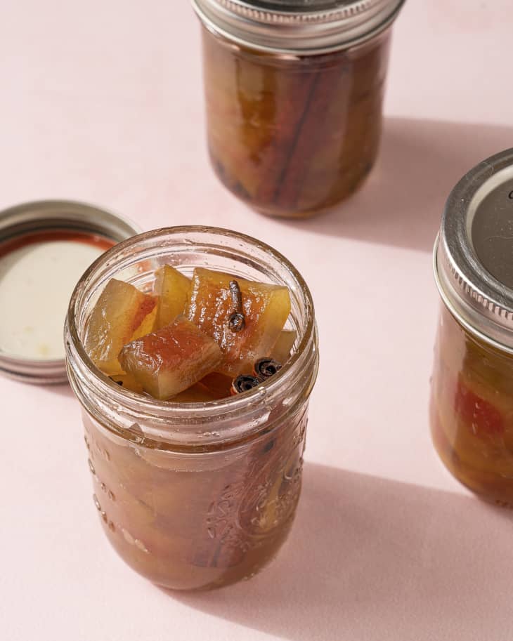 Pickled watermelon rind in a small glass jar with the lid off, and two other jars in the background.