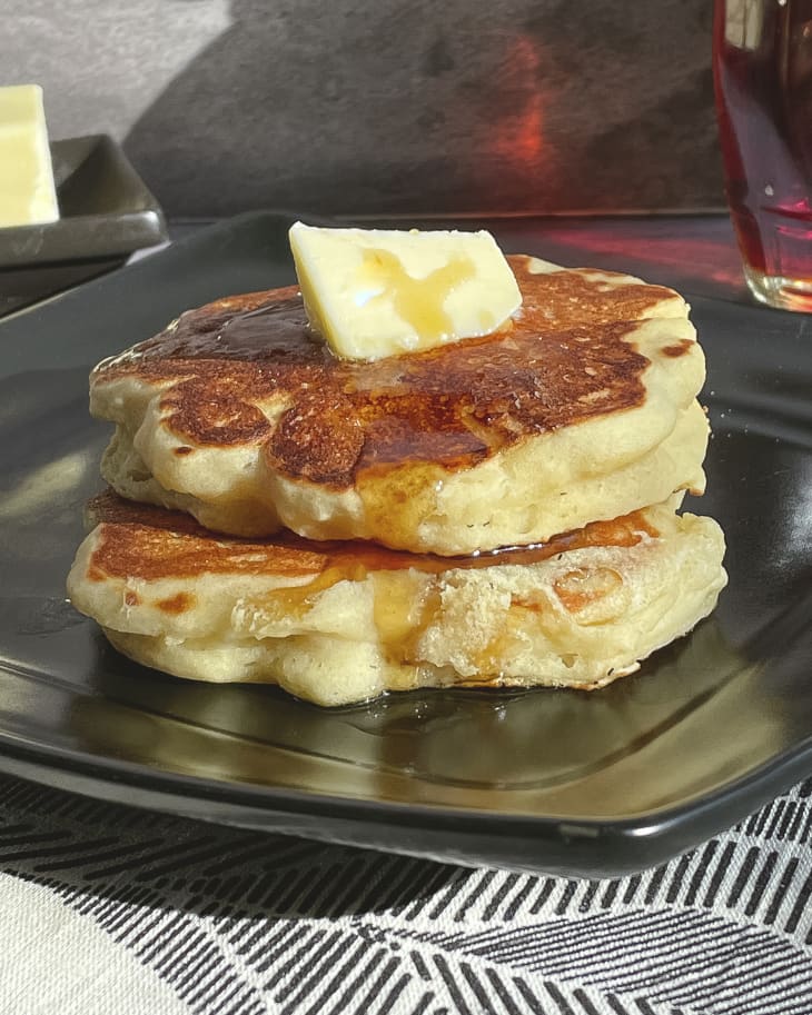 a photo of two thick griddle cakes with a pat of butter on top, on a square black plate.