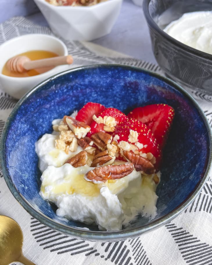 A photo of a bowl of greek yogurt with strawberries, pecans and honey over the top.