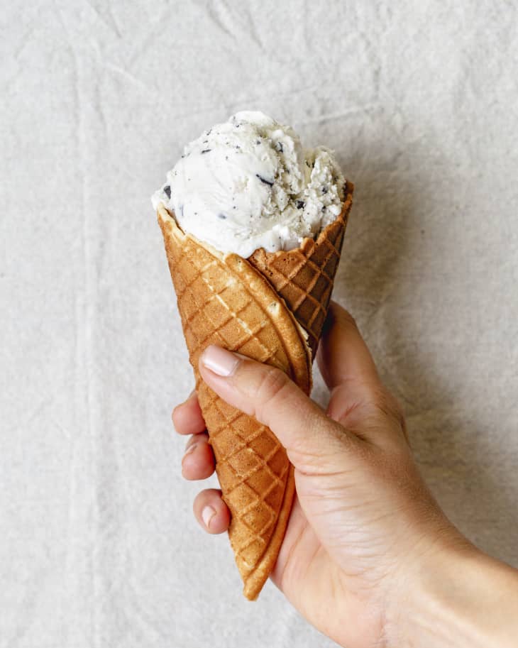 a hand holding an waffle cone with a scoop of white ice cream