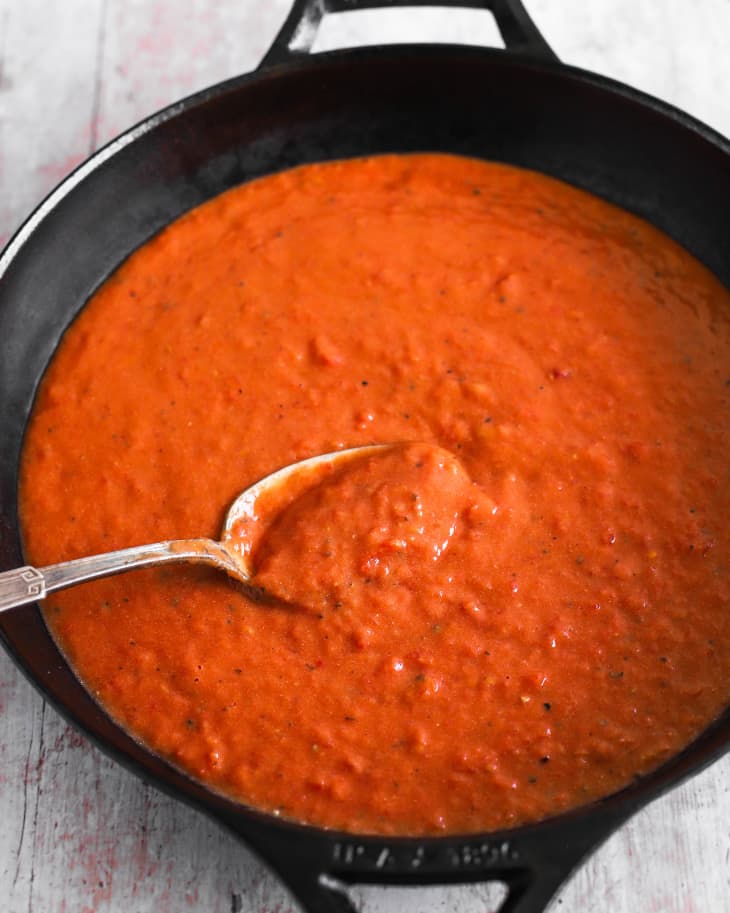 A photo of a black, round skillet with a thick, red tomato gravy in it and a spoon lifting some up.