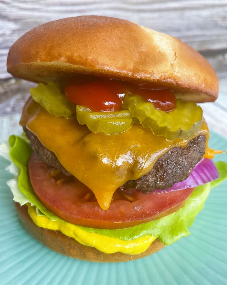A photo of a burger on a bun with ketchup, sliced pickles, lettuce tomato and red onion.