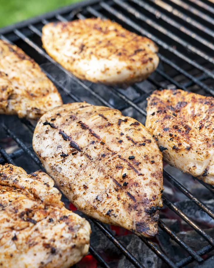 A photo of five pieces of grilled chicken breast on the grill.