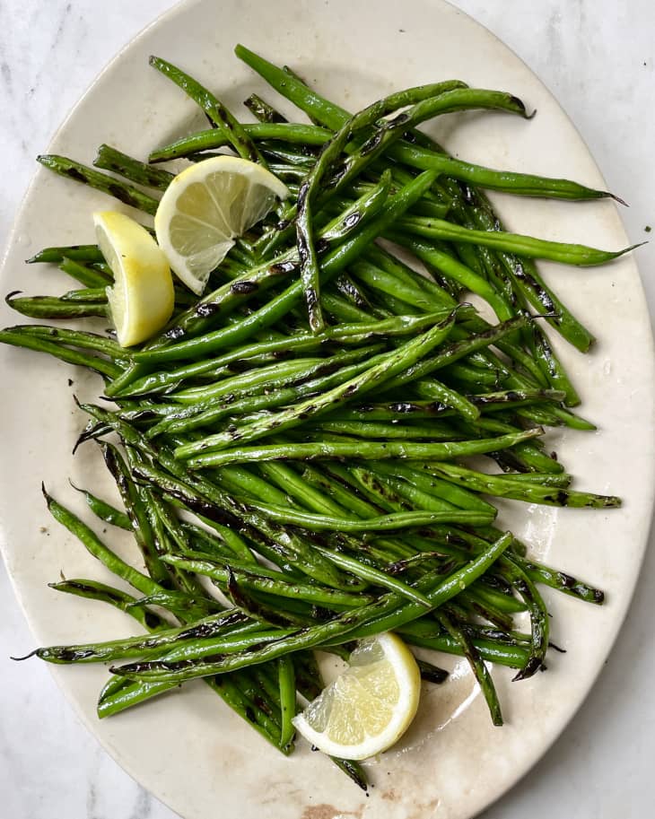 A photo of an oval white platter with grilled green beans and some lemon wedges