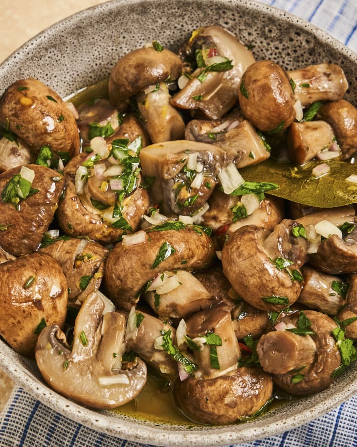A closeup photo of a bowl of marinated mushrooms with a green garnish sprinkled over the top.
