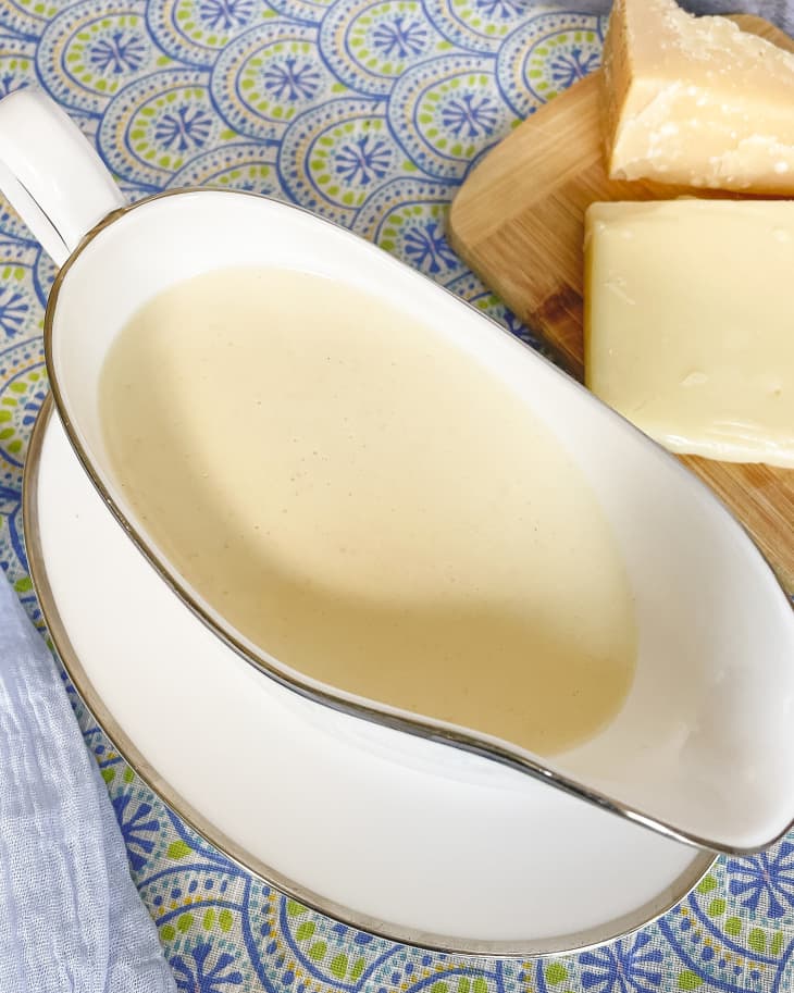 A  photo of a white sauce (Mornay sauce - a béchamel sauce with grated cheese added) in a gravy boat with some hard cheese on the side.