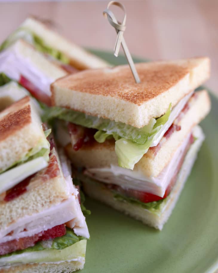 A photo of a club sandwich with toasted bread, lettuce, bacon, turkey and tomatoes, cut into triangular pieces.