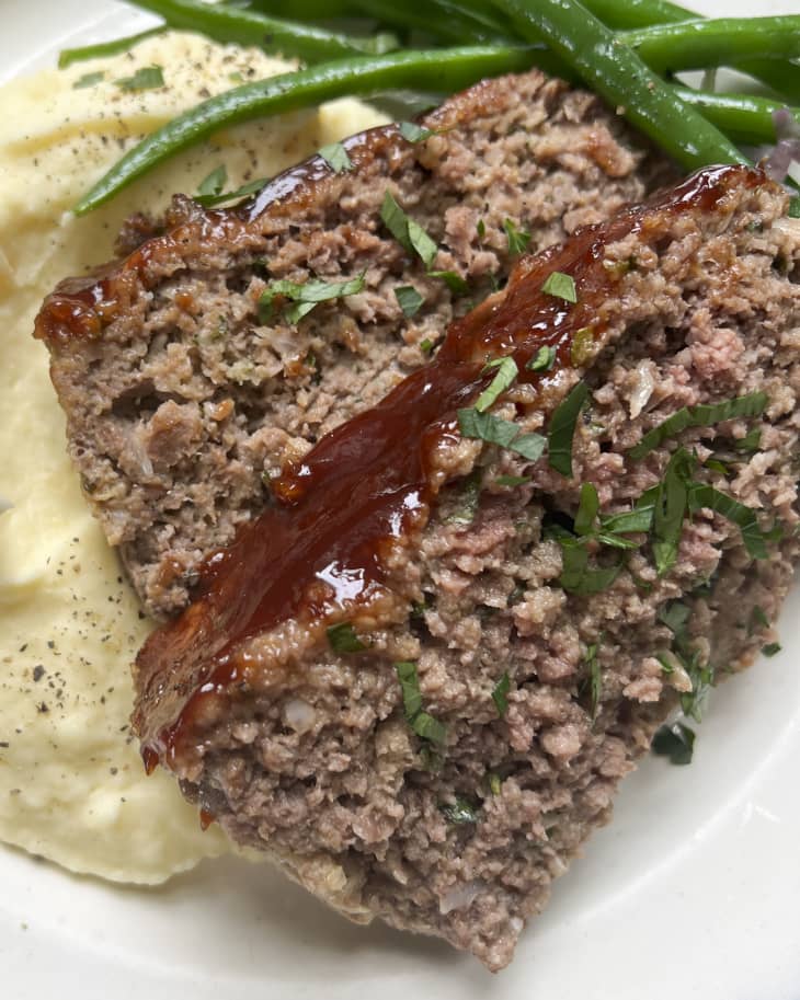 A photo of a slice of meatloaf on a plate with mashed potatoes and green beans.