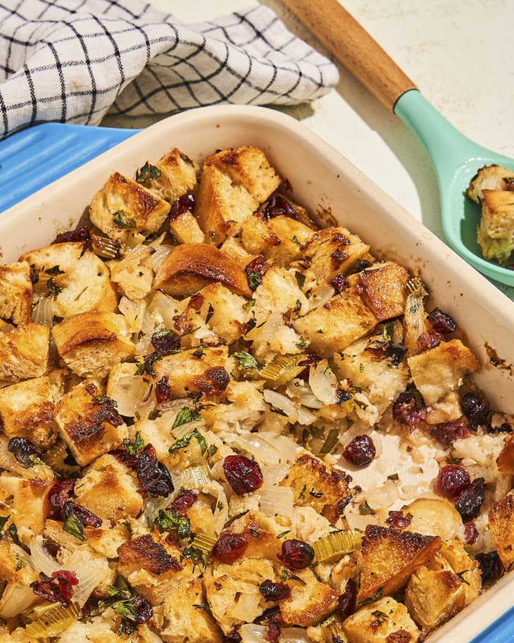 A photo of baked vegan stuffing in a square, porcelain baking dish with blue handles and a serving spoon with some of the stuffing on the side.