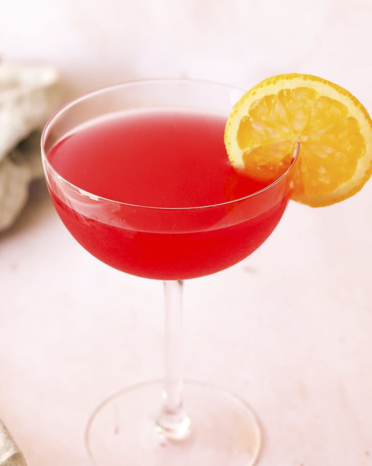 A photo of a bright red cosmopolitan cocktail with a lemon wedge on the side of the cocktail glass.