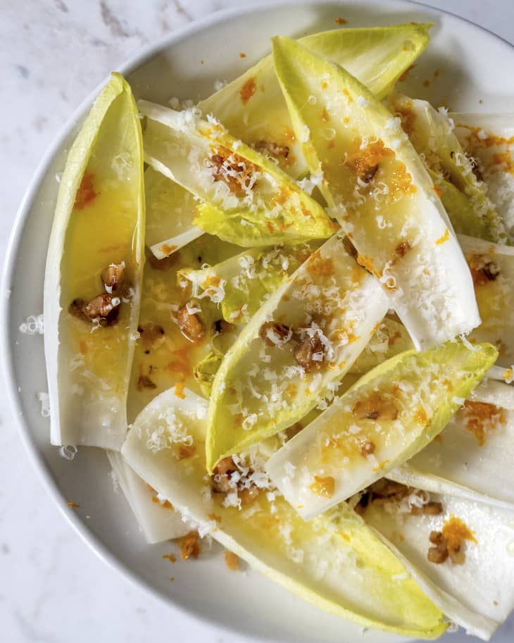 A photo of an endive salad with crushed nuts and shaved cheese on top.