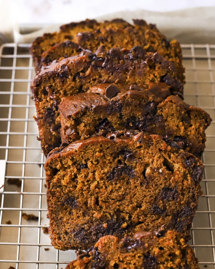 A photo of a sliced loaf of pumpkin chocolate chip bread on a cooling rack.