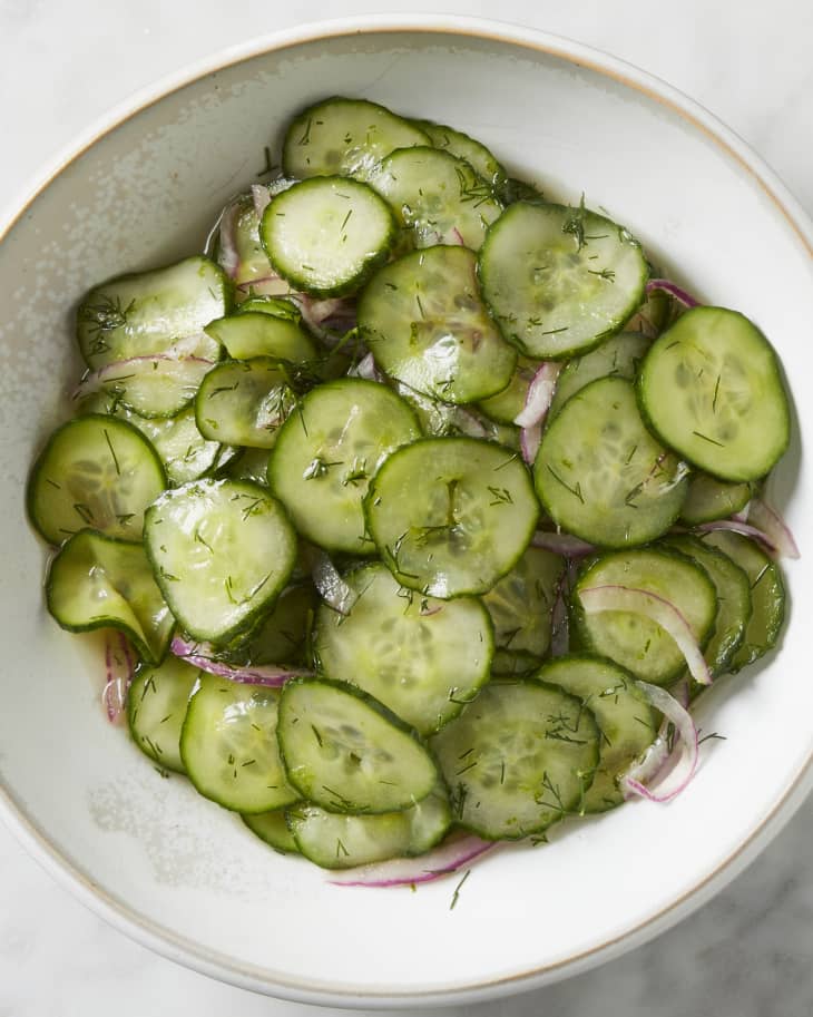 A bowl of cucumber onion salad on a marble surface.