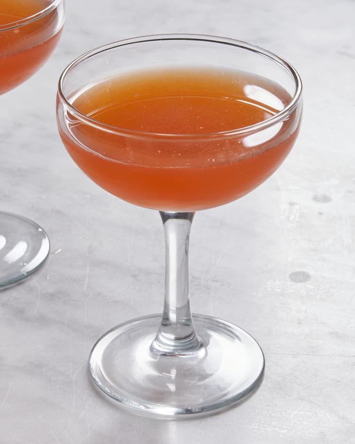 A coupe glass with a dark orange Paper Plane cocktail on a marble surface