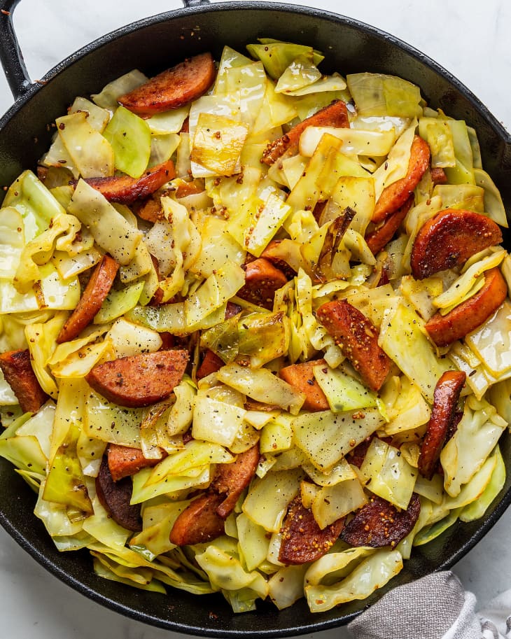 Overhead cast iron skillet with half-moon slices of kielbasa and buttery chopped green cabbage.
