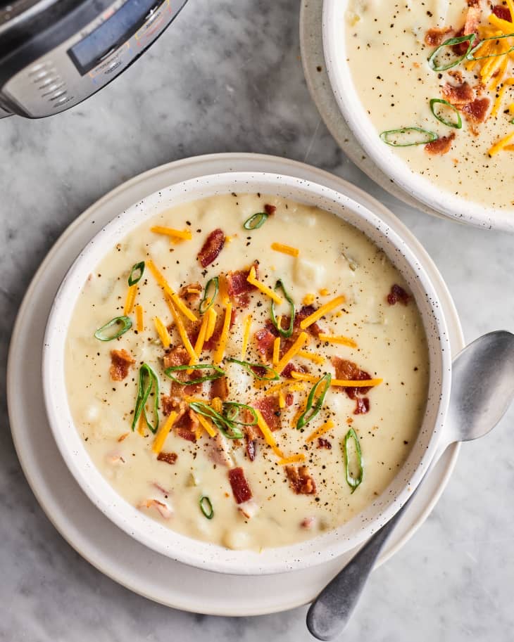 Two bowls of potato soup, topped with bacon, chives, and cheddar cheese