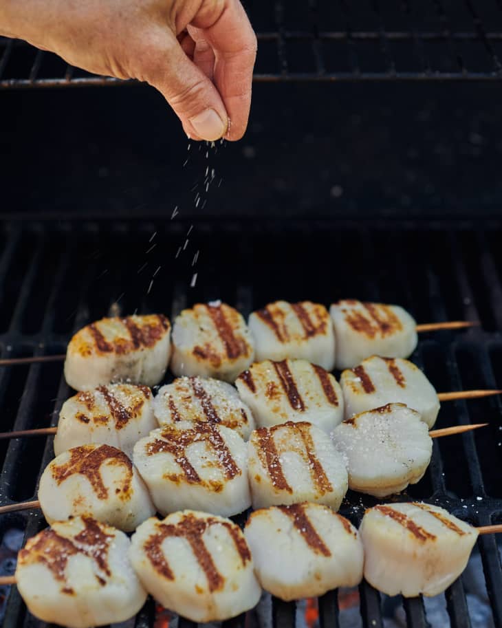 putting scallops on a skewer with butter melting in a saucepan on the grill