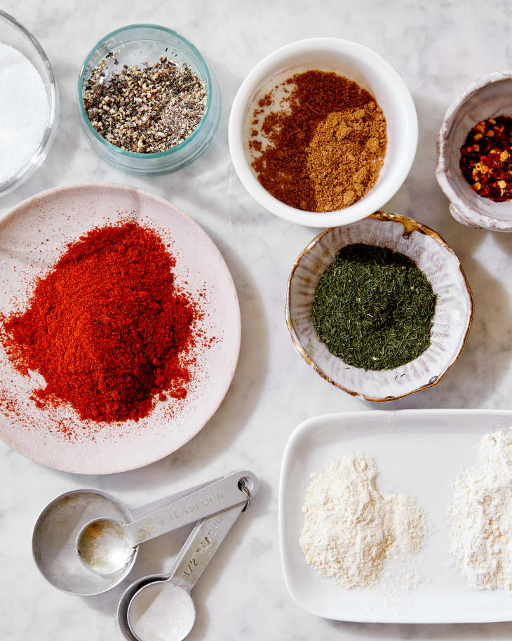 Spices are in individual bowls on a marble, kitchen surface.