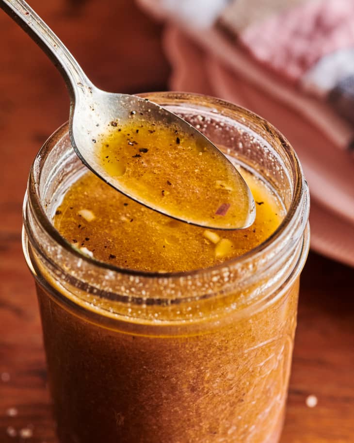 A spoon full of vinaigrette is emerging from a mason jar.