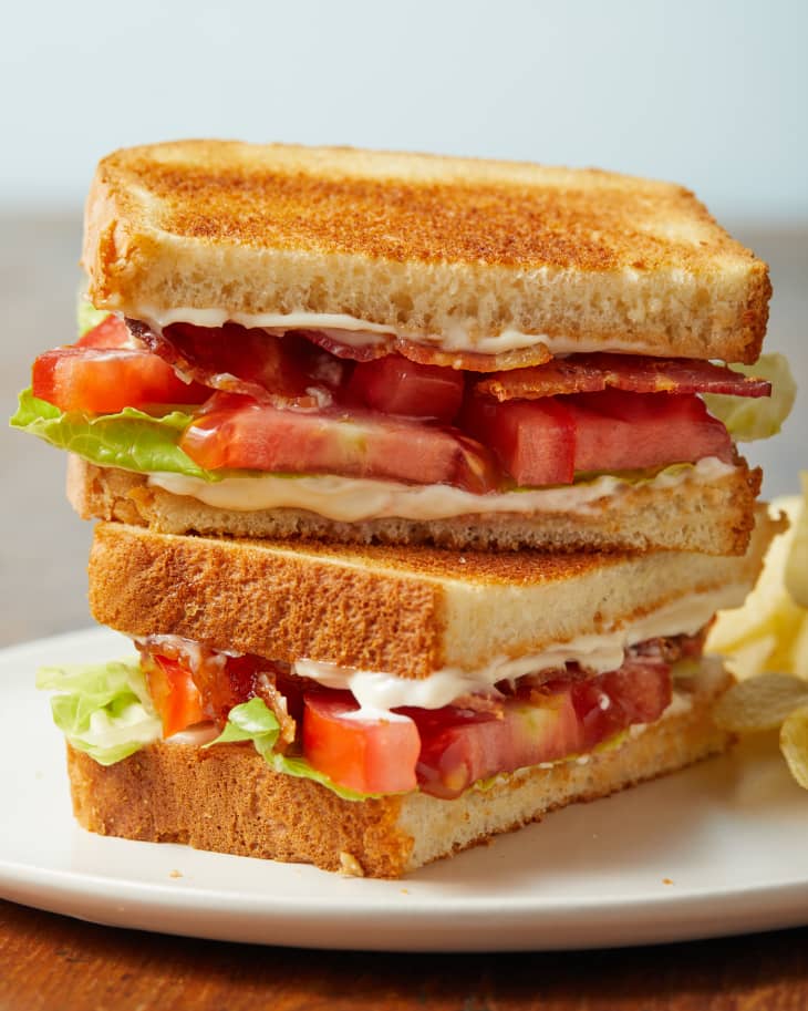 BLT sandwich cut in half and stacked on top of each other, placed on white plate