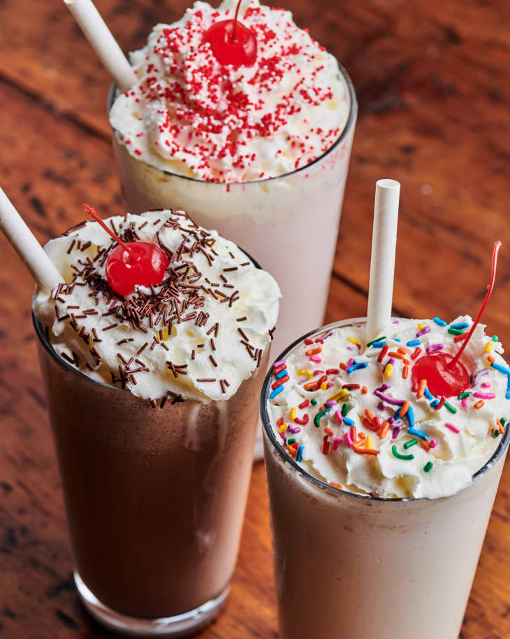 A strawberry milkshake, a chocolate milkshake, and a vanilla milkshake are topped with sprinkles and maraschino cherries.