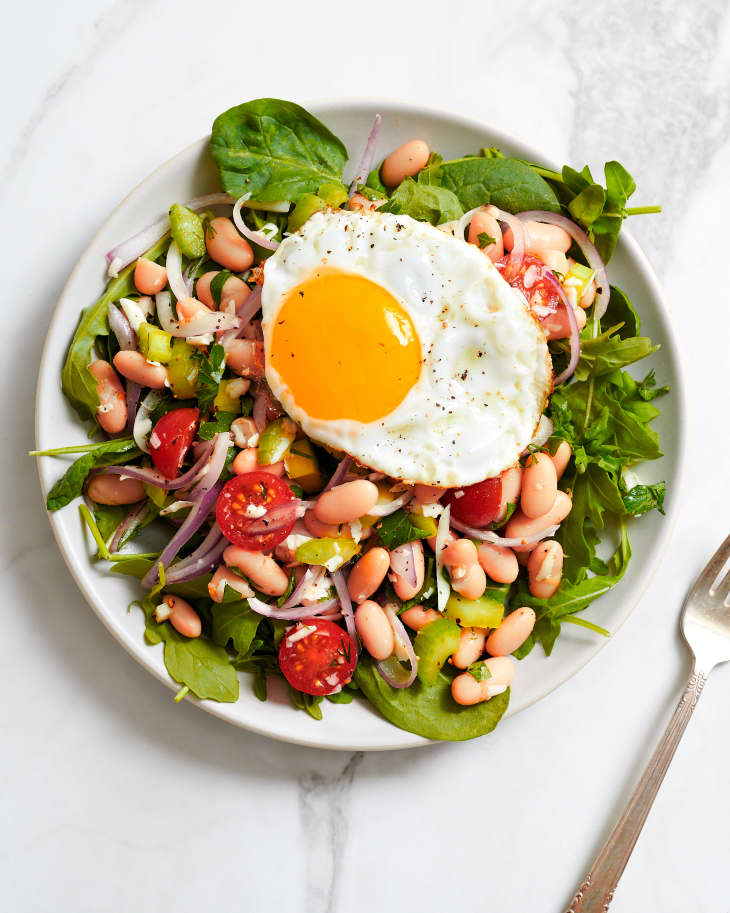 White bean salad on a bed of lettuce and topped with fried egg.