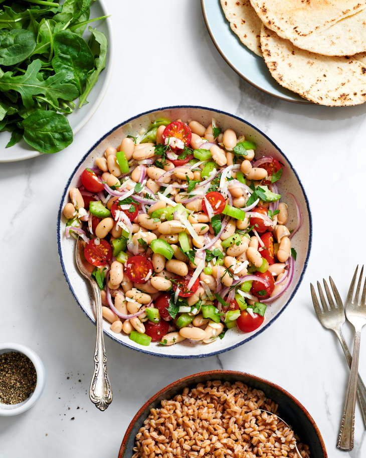 White bean salad surrounded by plates of fresh herbs, tortillas and farro.
