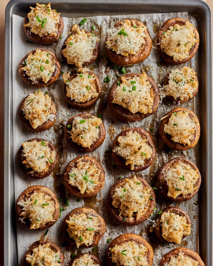 twenty crab stuffed mushroms are laid out on top of a grey baking sheet and parchment paper